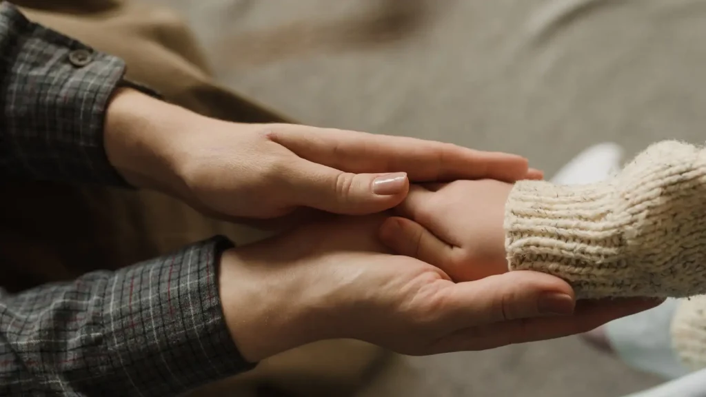 Adult gently holding a child’s hand in a comforting gesture.